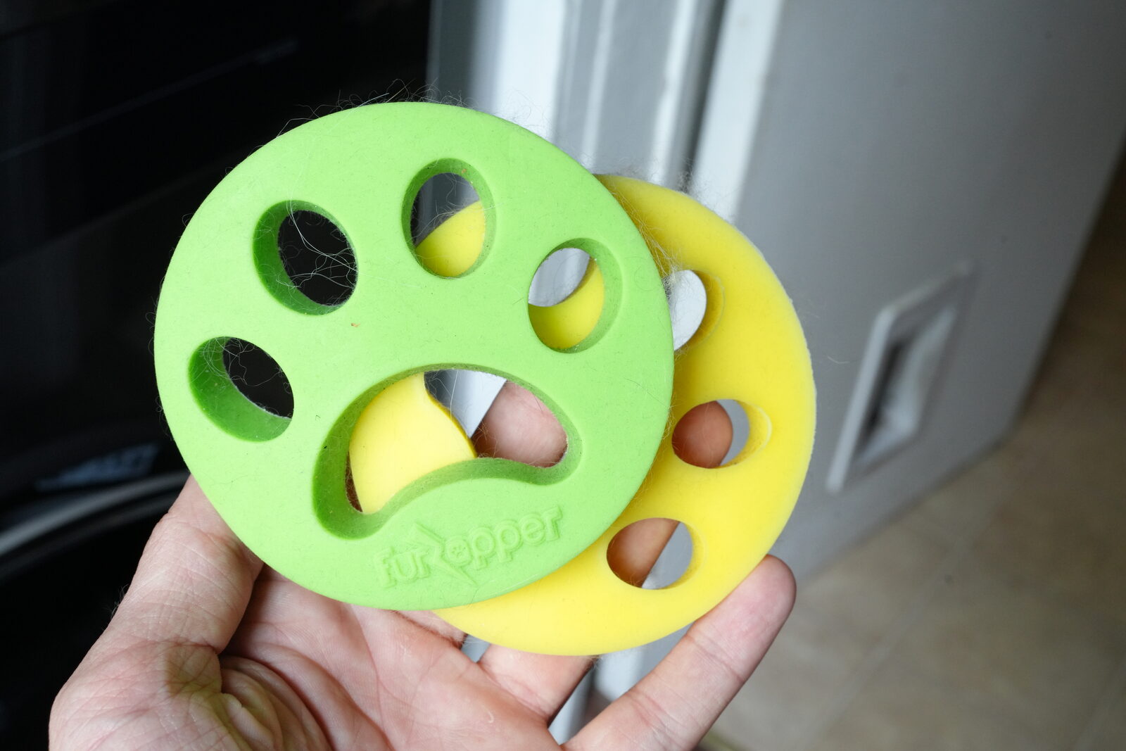 FurZapper silicone laundry discs in green and yellow paw shapes, held in hand near washer
